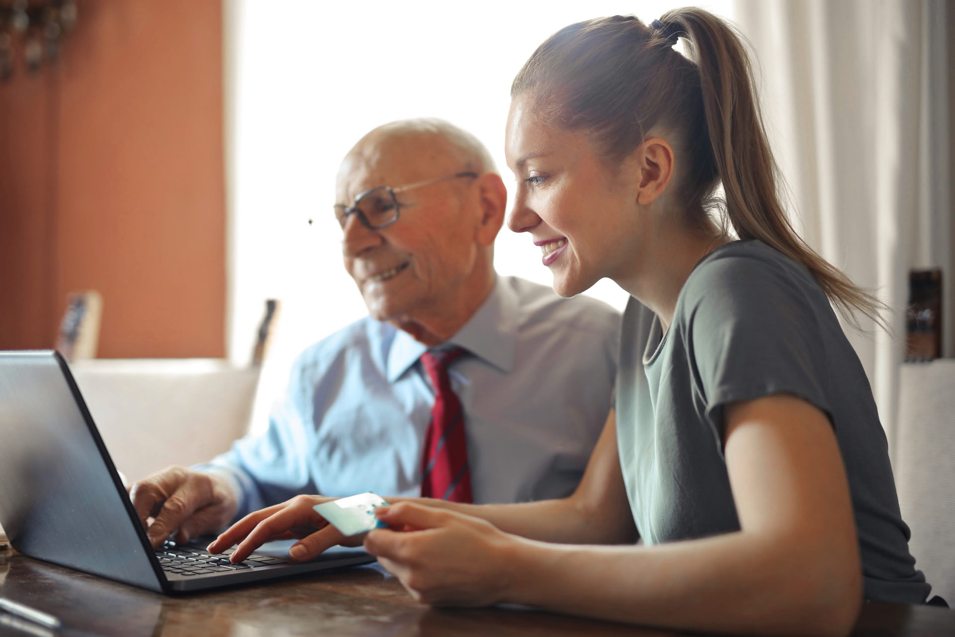 Canva - Young woman helping senior man with payment on Internet using laptop